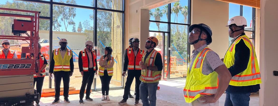 A group Cisco employees and UC Riverside employees wearing hard hats and safety vests inside of the construction site of the SoCal OASIS Park building.