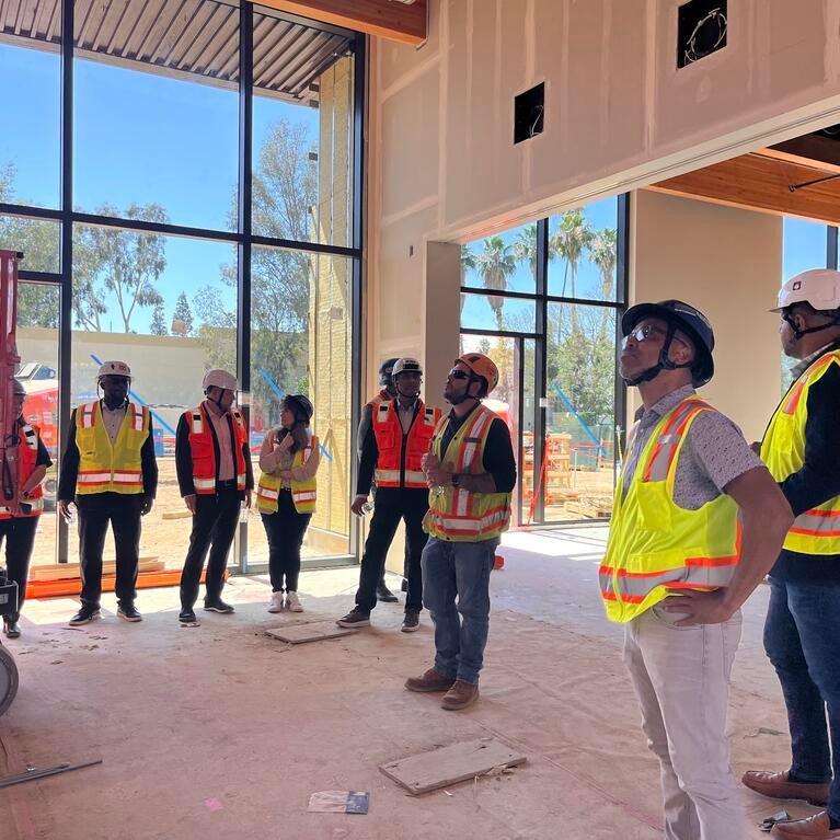 A group Cisco employees and UC Riverside employees wearing hard hats and safety vests inside of the construction site of the SoCal OASIS Park building.