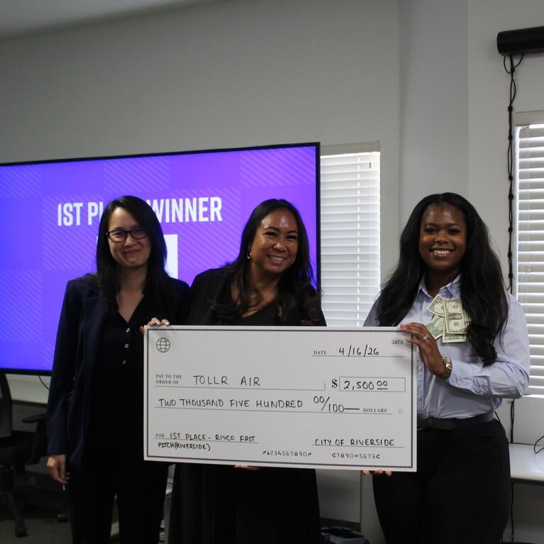 1st Place Winner of 2026 RivCo Fast Pitch Riverside Regional, Keziyah Yisrael-Gayle, representing TollR, pictured with Jennifer Yturralde of UC Riverside and Tiffany Yu of Riverside County, holding a large check of $2,500.