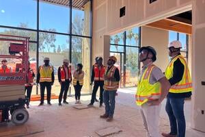 A group Cisco employees and UC Riverside employees wearing hard hats and safety vests inside of the construction site of the SoCal OASIS Park building.
