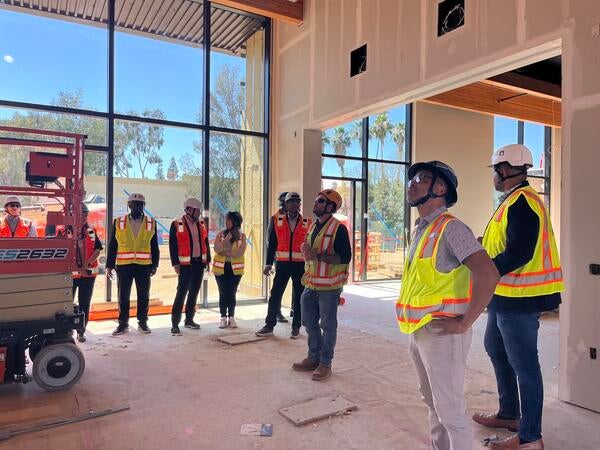 A group Cisco employees and UC Riverside employees wearing hard hats and safety vests inside of the construction site of the SoCal OASIS Park building.