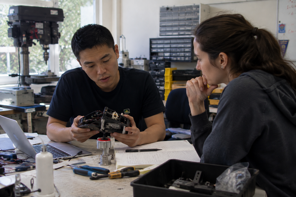 Picture of innovator showing his technology invention to a woman. Both of them are sitting at a table in a workshop.